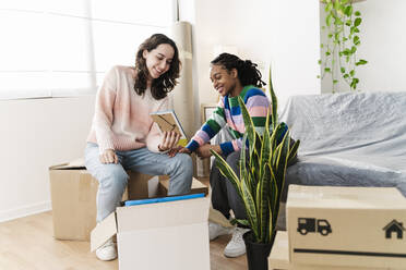 Happy multiracial friends looking at frame in home - JCZF01169