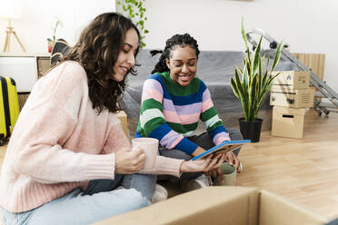 Happy multiracial young friends looking at photo frame in living room - JCZF01175