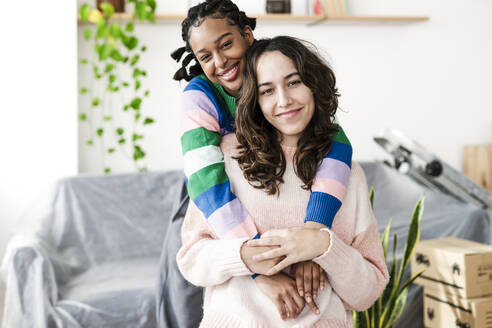 Smiling young woman embracing friend at home - JCZF01188