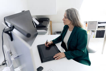 Geschäftsfrau mit Grafiktablett an einem Schreibtisch im Büro sitzend - FLLF00834