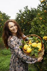 Happy redhead woman standing with basket of oranges - NJAF00212