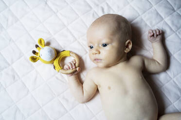 Shirtless baby boy with toy lying on bed at home - NJAF00231