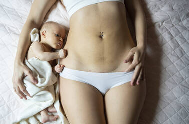 Baby boy lying next to mother with caesarean scar on belly - NJAF00234