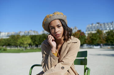 Young woman wearing beret sitting on chair in front of blue sky - KIJF04520