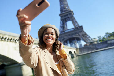Glückliche junge Frau macht ein Selfie mit ihrem Smartphone vor dem Eiffelturm, Paris, Frankreich - KIJF04538