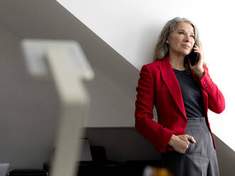 Geschäftsfrau, die im Büro mit einem Smartphone telefoniert - FLLF00845