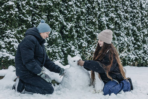 Lächelnde Freunde bauen Schneemann im Winter im Park - VSNF00412