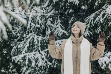 Young woman wearing warm clothing in snowfall at park - VSNF00419