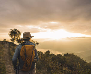 Frau mit Hut beim Wandern auf einem Berg bei Sonnenuntergang - UUF28180