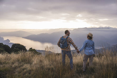Happy mature couple holding hands standing on mountain - UUF28203