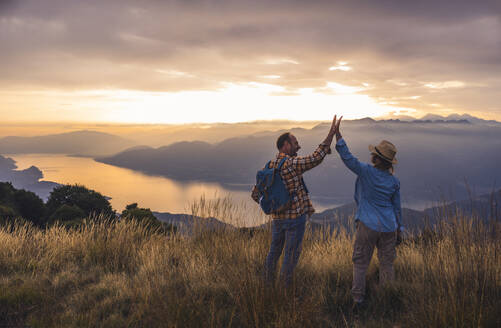 Happy man and woman giving high-five to each other standing on mountain - UUF28212