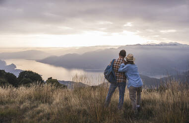 Mature man and woman standing on mountain at sunset - UUF28213