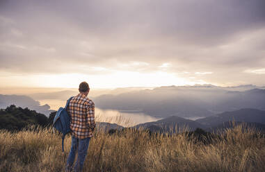 Älterer Mann mit Rucksack steht auf einem Berg bei Sonnenuntergang - UUF28215