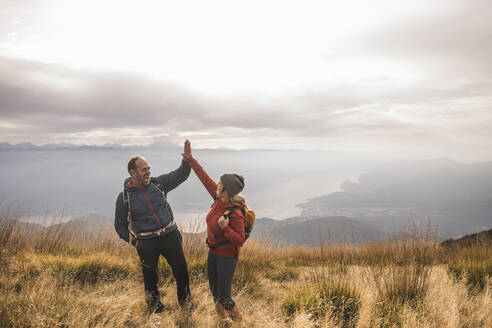 Cheerful man and woman giving high-five to each other standing on mountain - UUF28240