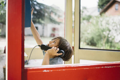 Neugieriger Junge greift in einer Telefonzelle nach den Tasten - ANAF00979