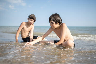 Brüder spielen zusammen im nassen Sand am Strand sitzend - ANAF00988