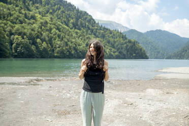 Lächelnde Frau vor einem See stehend - ANAF00990