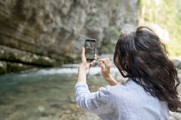 Frau fotografiert Klippe durch Smartphone im Urlaub - ANAF00993