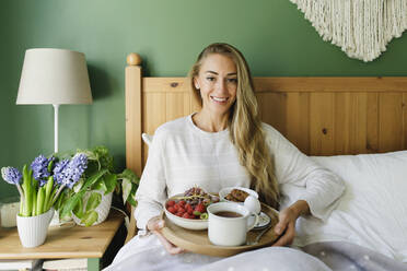 Happy woman sitting with breakfast in bed at home - TYF00700