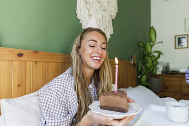 Glückliche Frau mit einem Stück Kuchen, die ihren Geburtstag zu Hause feiert - TYF00709