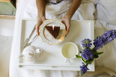 Woman with slice of cake celebrating birthday on bed - TYF00710