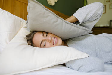 Woman closing ears with pillow in bed at home - TYF00718