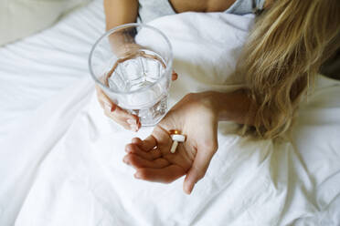 Frau nimmt Tabletten mit einem Glas Wasser im Bett zu Hause - TYF00724