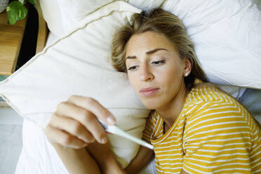 kranke Frau, die zu Hause im Bett die Temperatur mit einem Thermometer überprüft - TYF00726