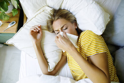 Kranke Frau wischt sich im Bett zu Hause die Nase mit einem Taschentuch ab - TYF00727