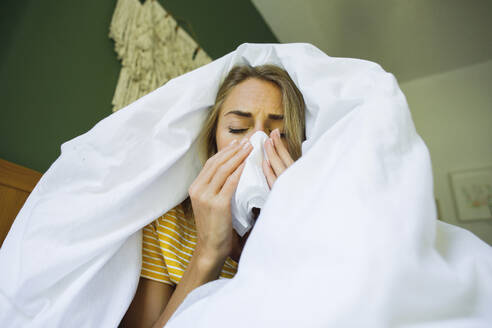 Frau unter Decke wischt sich die Nase mit einem Taschentuch im Bett zu Hause ab - TYF00728
