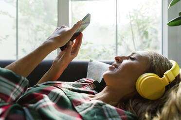 Frau, die ein Smartphone benutzt und zu Hause über Kopfhörer Musik hört - TYF00737