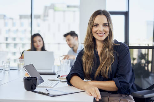 Lächelnde Geschäftsfrau mit Kollegen im Hintergrund im Büro - BSZF02038