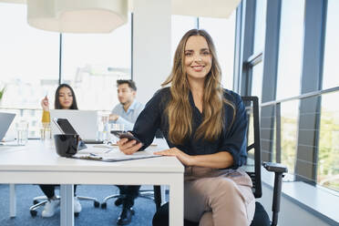 Smiling businesswoman sitting at desk in office - BSZF02039