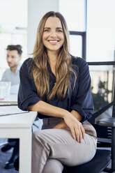 Happy businesswoman sitting on chair at office - BSZF02040