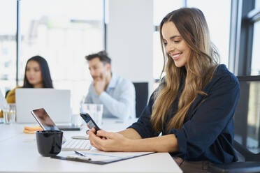 Smiling businesswoman using mobile phone at desk in office - BSZF02041
