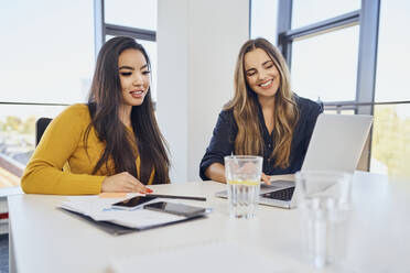 Smiling business colleagues working together over laptop at workplace - BSZF02043