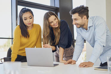 Happy businesswoman discussing with colleagues over laptop at workplace - BSZF02046