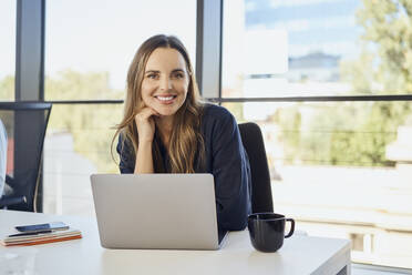 Smiling businesswoman with laptop at office - BSZF02082