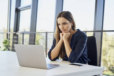 Businesswoman watching laptop sitting at desk in office - BSZF02085