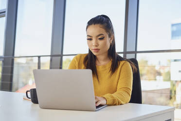 Junge Geschäftsfrau arbeitet am Laptop am Schreibtisch im Büro - BSZF02088