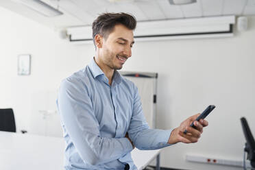 Lächelnder Geschäftsmann, der ein Mobiltelefon am Arbeitsplatz benutzt - BSZF02107