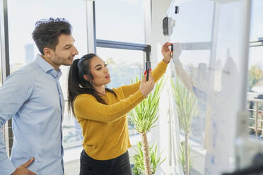 Geschäftsfrau, die ein Smartphone neben einem Kollegen und einem Whiteboard im Büro benutzt - BSZF02115