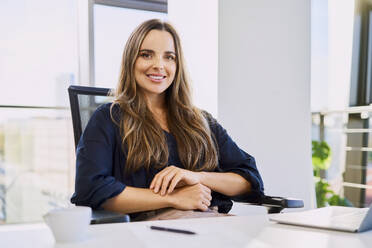 Confident businesswoman sitting on chair at desk in office - BSZF02132