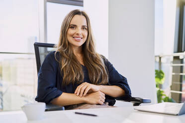 Selbstbewusste Geschäftsfrau sitzt auf einem Stuhl am Schreibtisch im Büro - BSZF02132