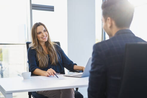 Smiling recruiter discussing with candidate at office - BSZF02134