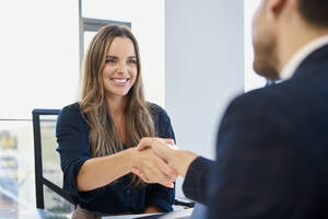 Glückliche Geschäftsfrau schüttelt Hand mit Geschäftsmann nach Interview im Büro - BSZF02137