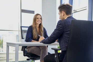 Lächelnder Personalverantwortlicher bei einem Vorstellungsgespräch mit einem im Büro sitzenden Bewerber - BSZF02140