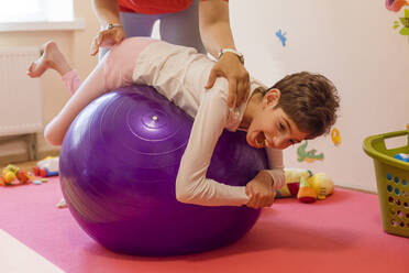 Physical therapist helping girl with disability in exercising on fitness ball at rehabilitation centre - OSF01381