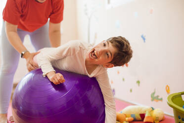 Physiotherapeutin hilft einem Mädchen mit Behinderung, das in einem Rehabilitationszentrum auf einem Fitnessball liegt - OSF01382