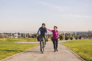 Man riding bicycle with woman running on road - JCCMF09334
